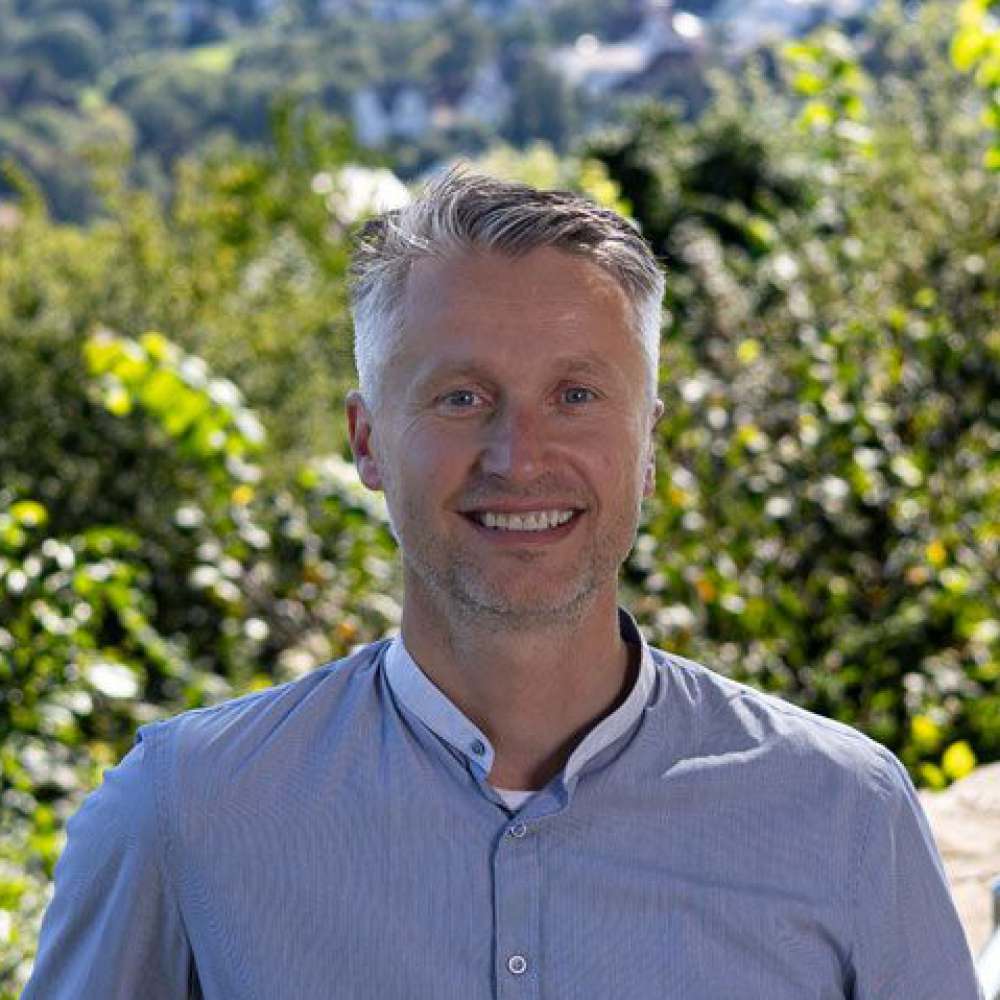 Ein junger Mann steht lächelnd draußen 