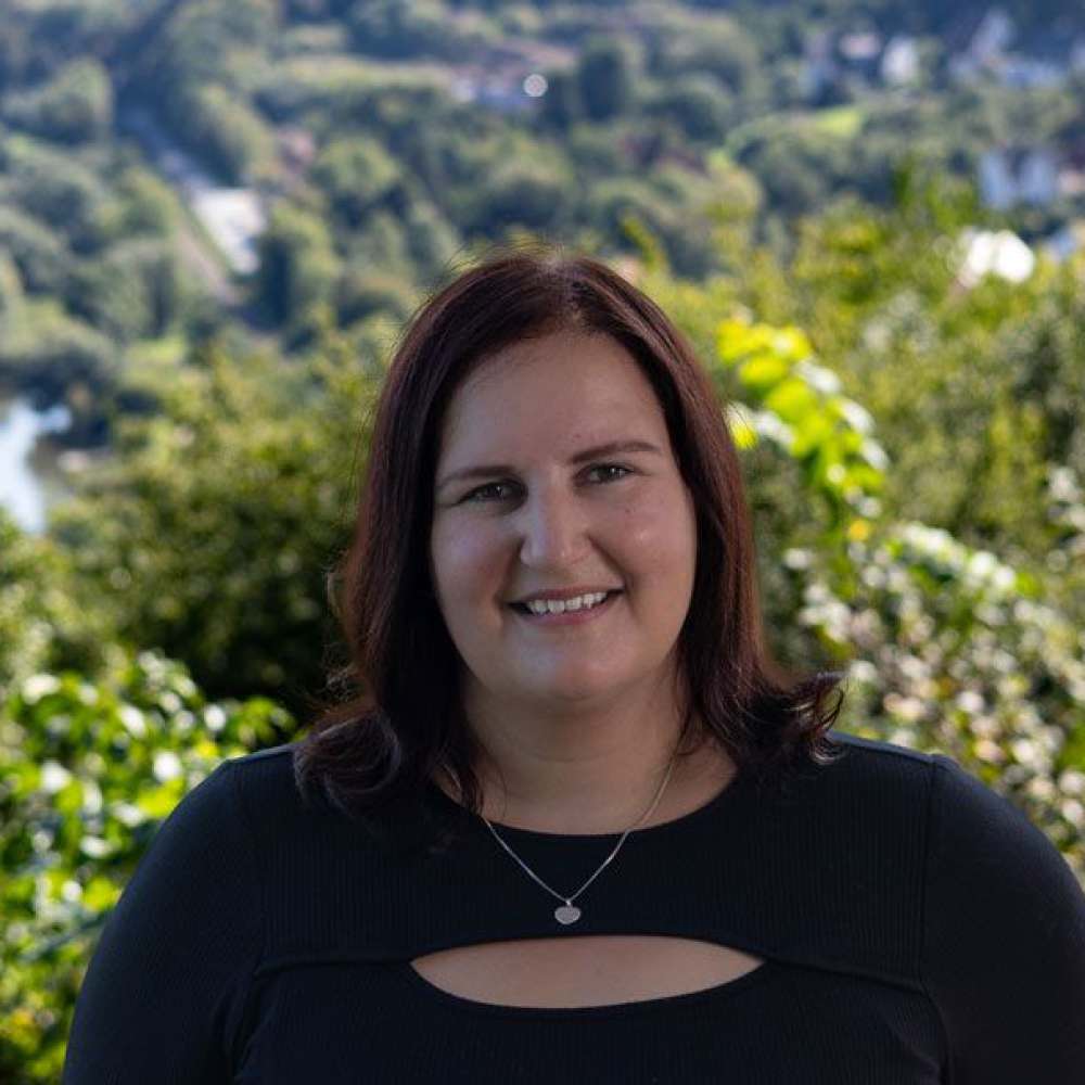  Ein junge Frau steht lächelnd draußen vor einer Mauer