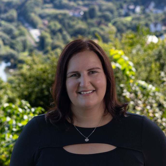  Ein junge Frau steht lächelnd draußen vor einer Mauer